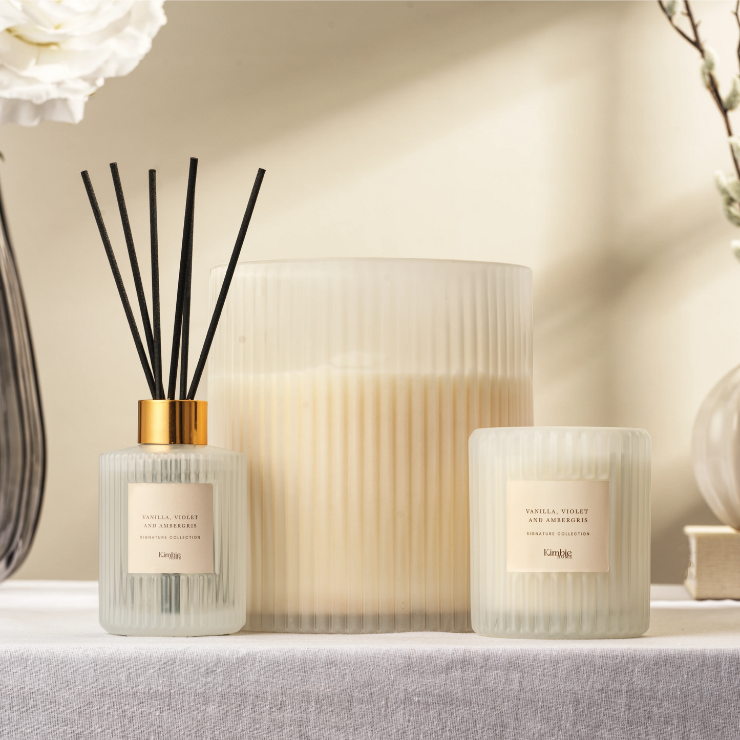 Decorative collection of soy wax candles and natural oil diffuser in white glass.