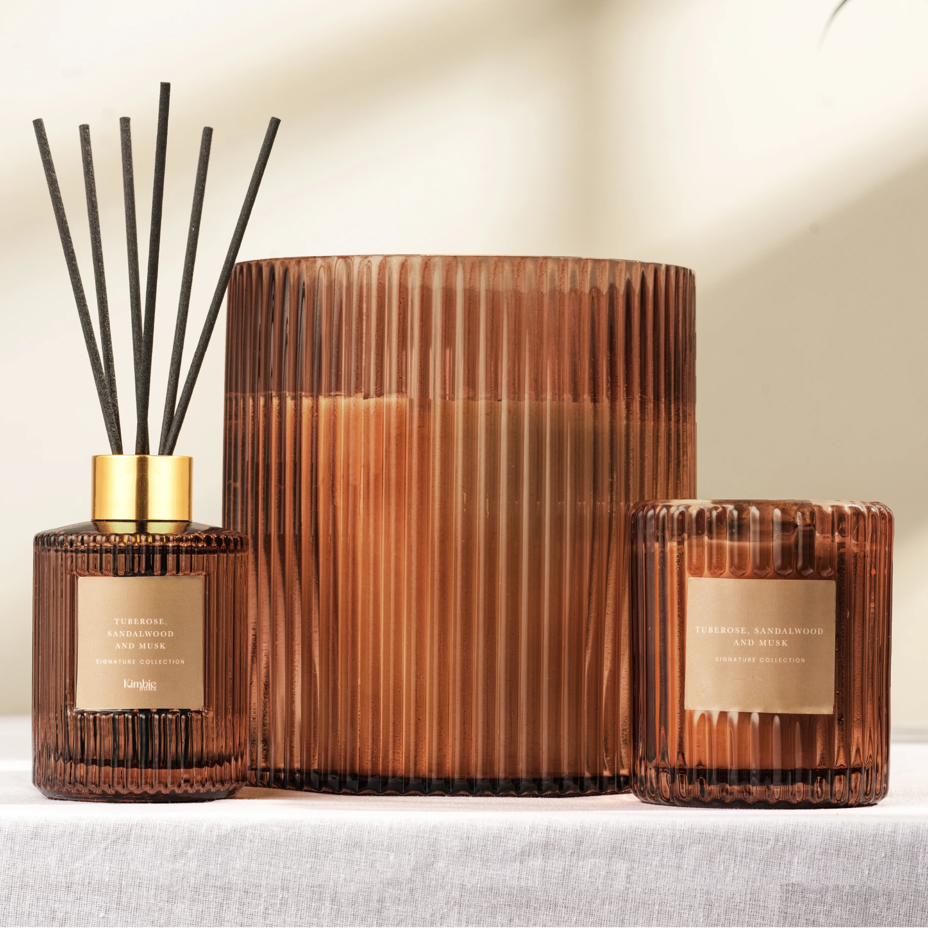 Decorative collection of ribbed glass soy wax candles and natural oil diffuser on a neutral background