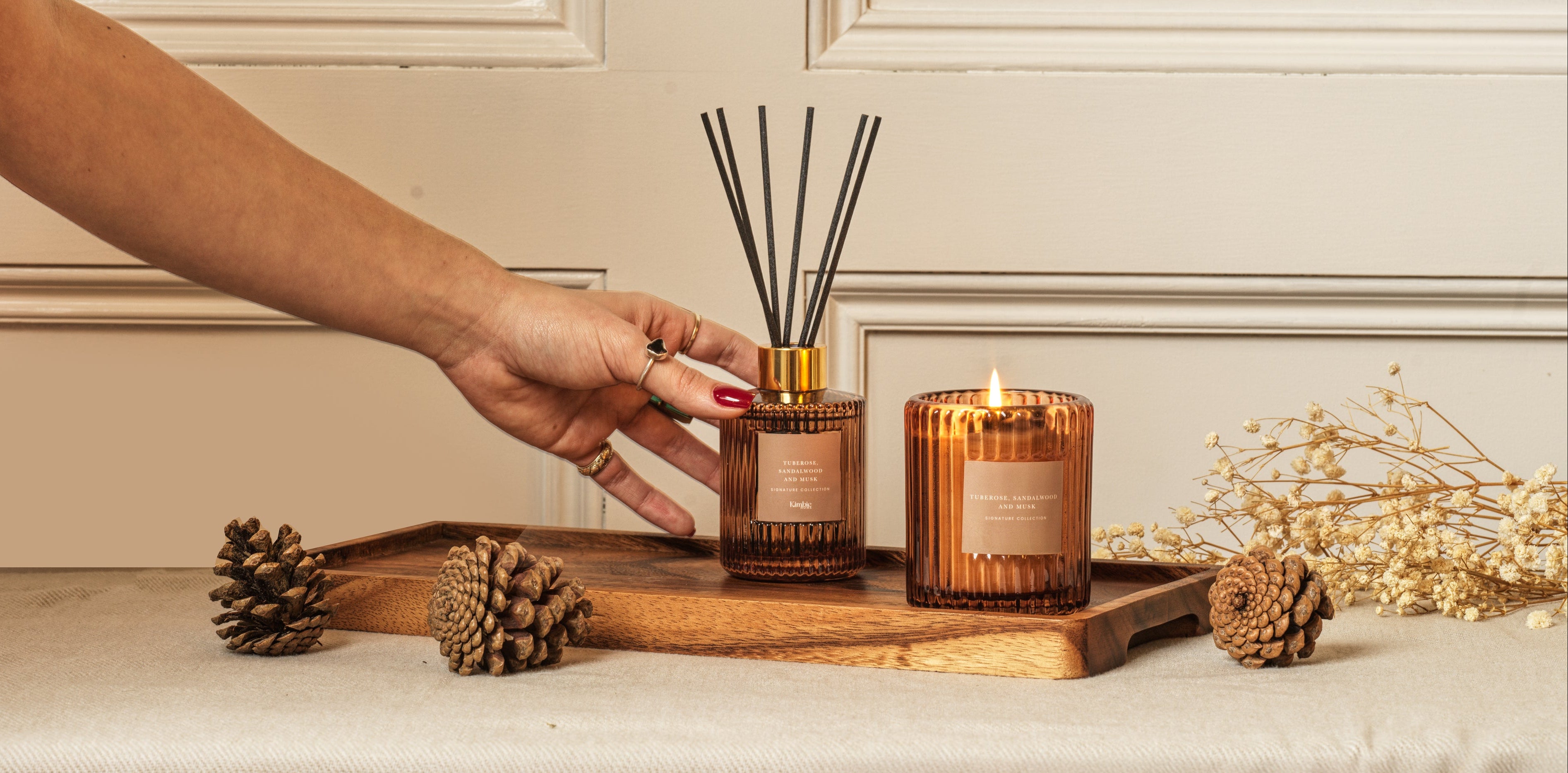 Hand reaching for a diffuser on a wooden tray with candles and decorative elements.
