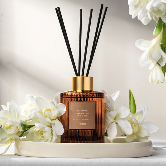 A natural oil diffuser with black sticks on a white tray surrounded by white flowers on a light background