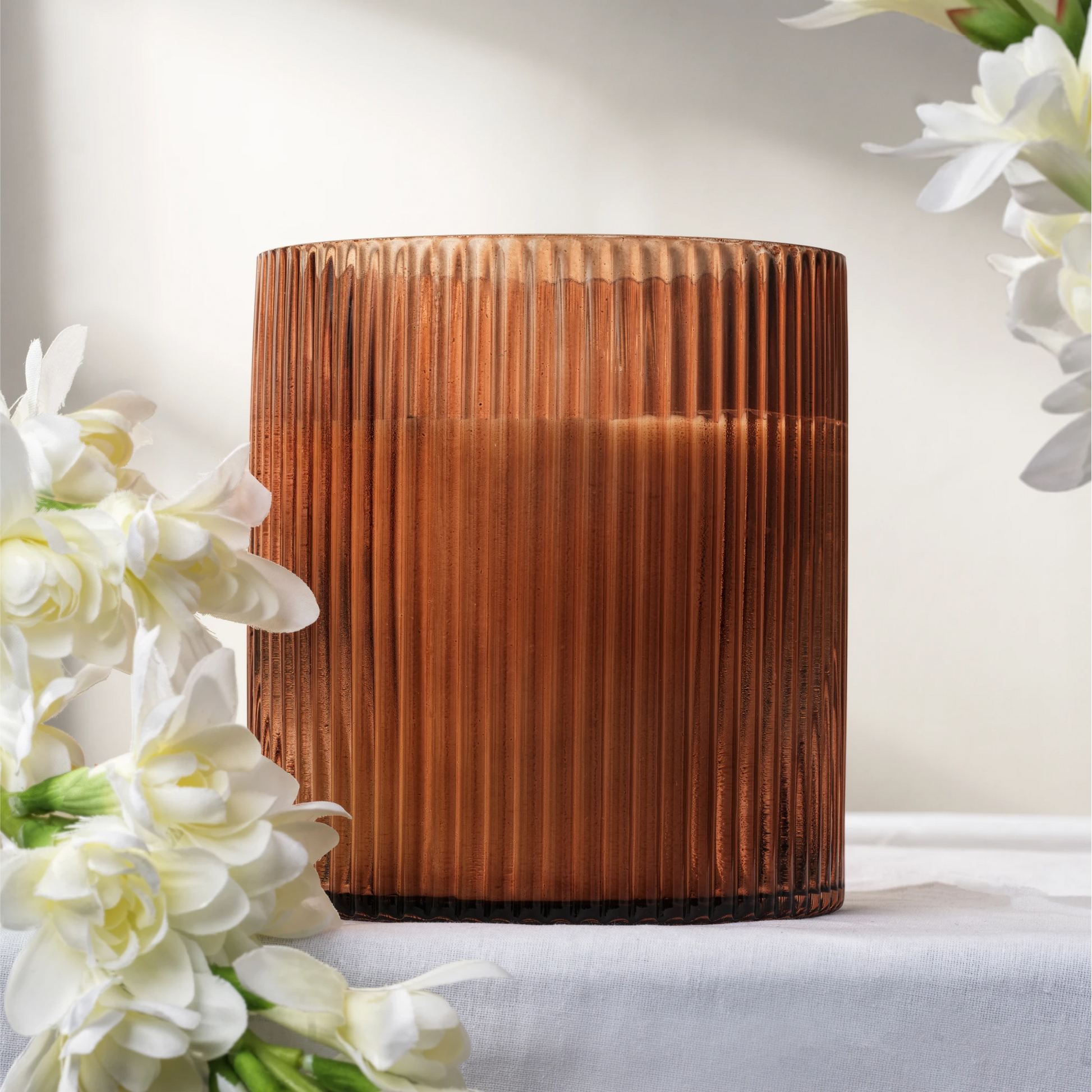 Amber glass ribbed soy wax candle with white flowers on a light background