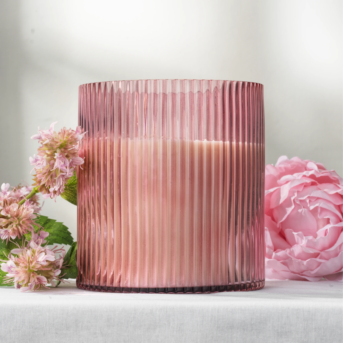 Pink ribbed glass soy wax candle with pink flowers on a light background
