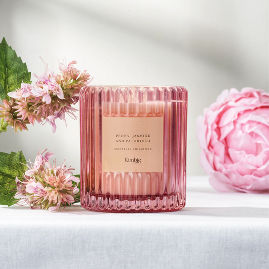 Pink ribbed glass soy wax candle with floral arrangement on a white surface