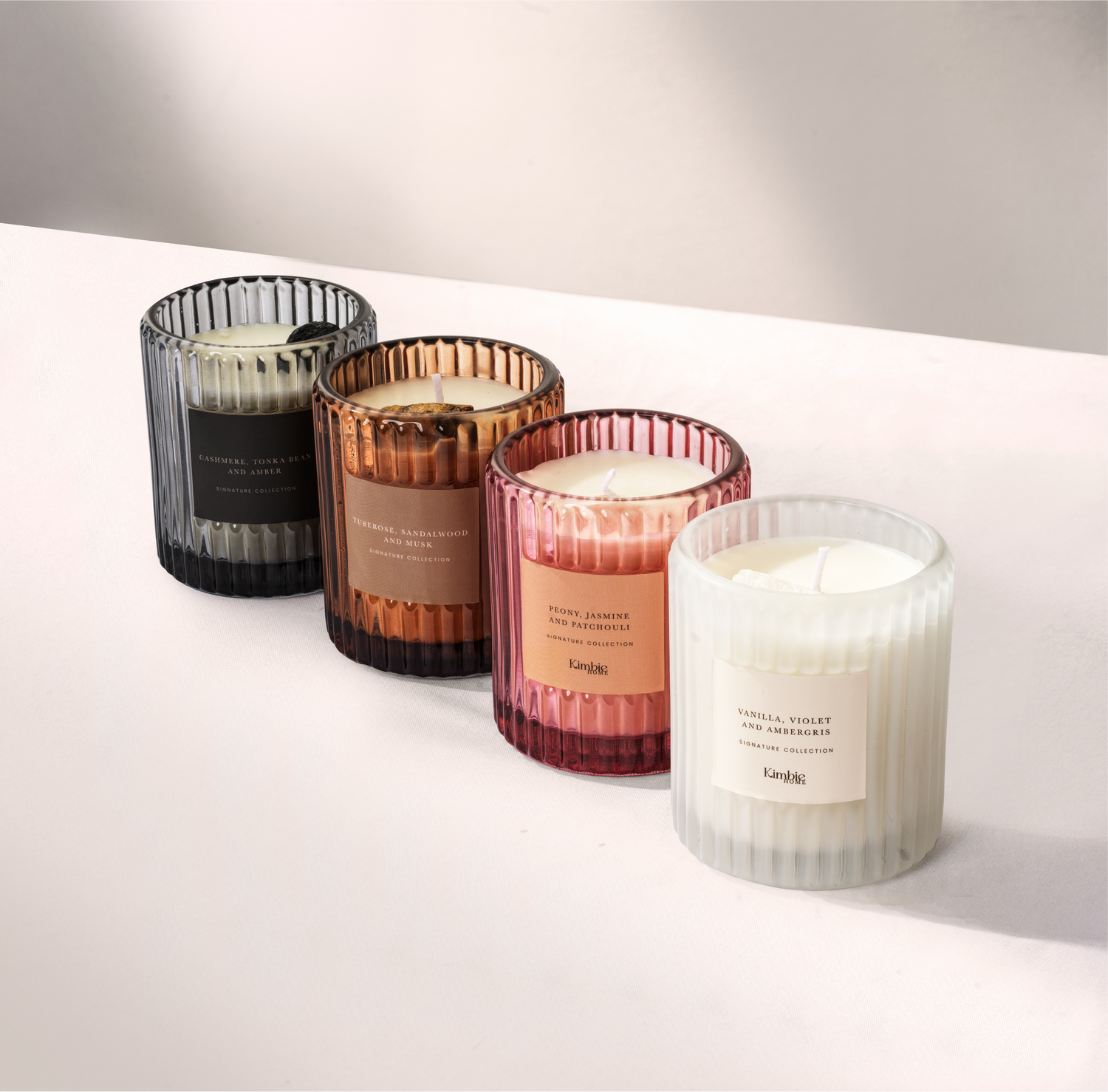 Set of four soy wax candles with coloured glass holders on a white surface