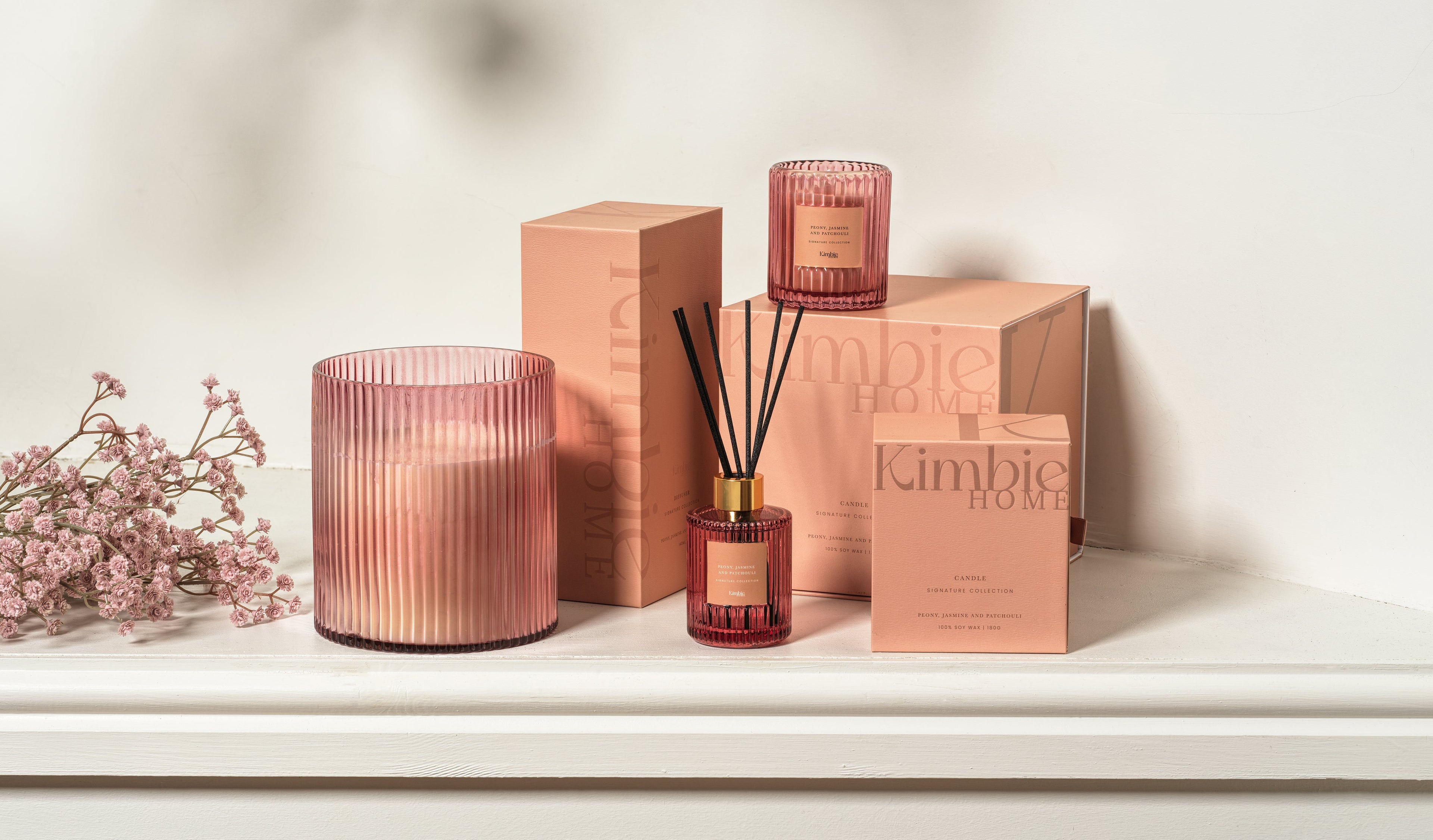 Collection of pink kimbie soy wax candles and natural oil diffusers on white background.